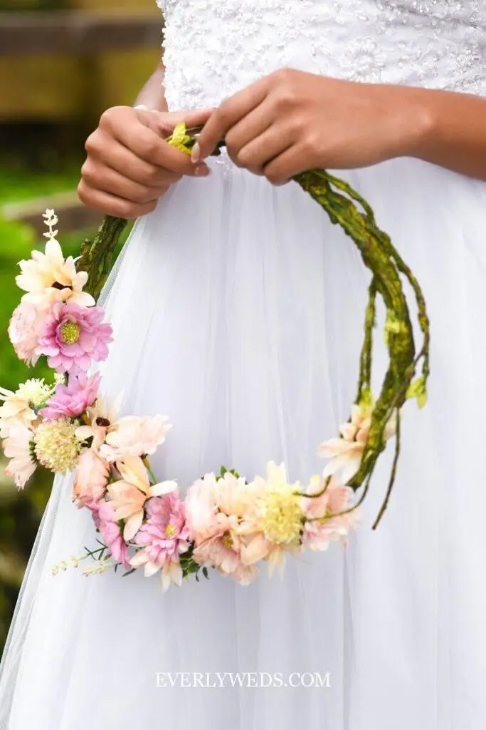 bridesmaid holding floral hoop wreath with greenery and flowers as boho bridesmaid bouquet alternative at garden wedding