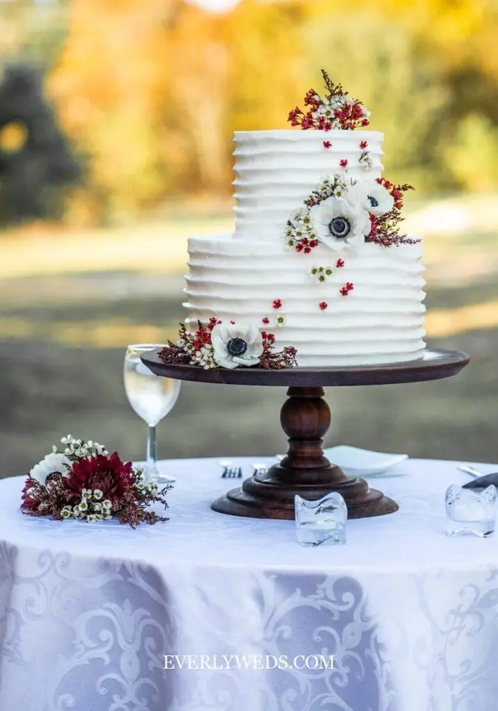 Simple wedding cake with flowers, fresh garden roses and eucalyptus cascading between two tiers on a white linen table