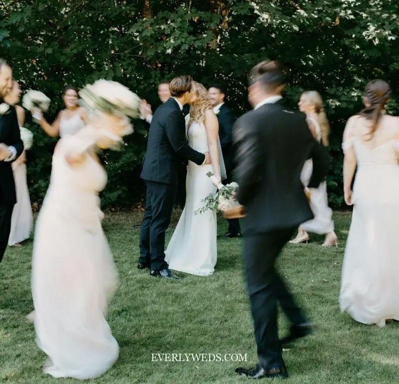 Bride and groom kissing at outdoor wedding celebration with guests - save the date ideas inspiration