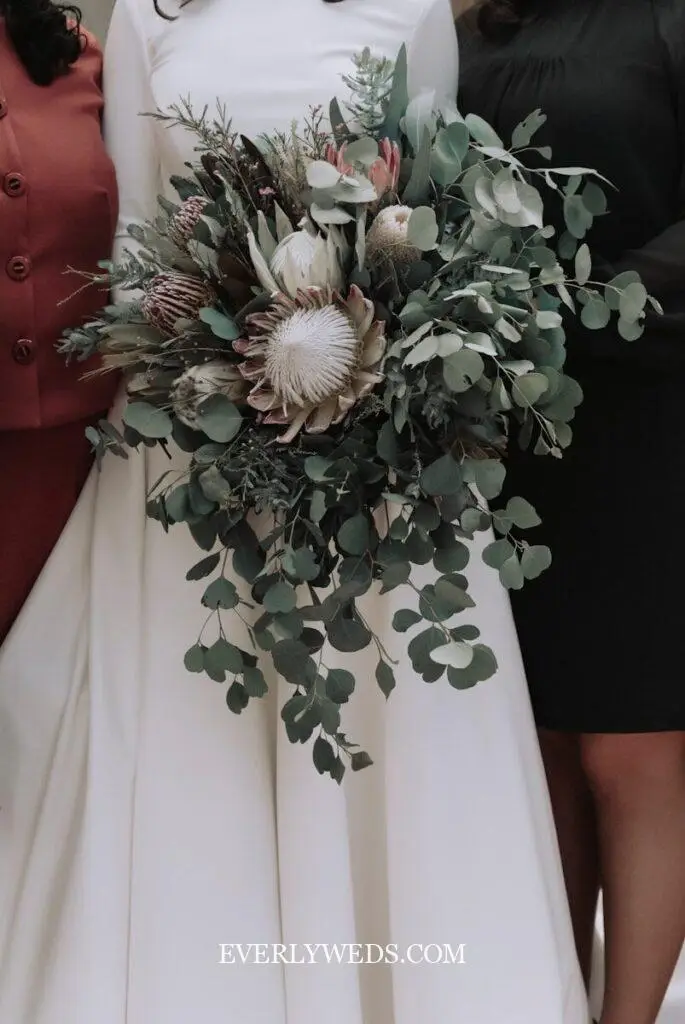 Green wedding theme flowers including eucalyptus bouquet with white peonies, fern garlands, and monstera leaf floral arrangements for ceremony arch decor