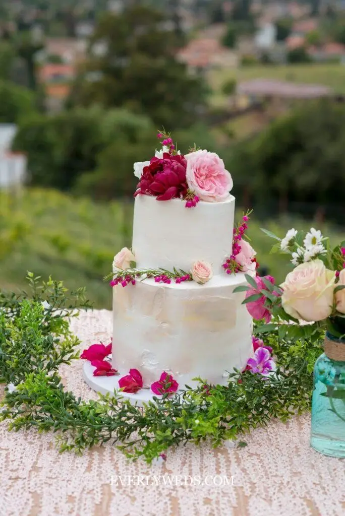 two tier wedding cake design with elegant white buttercream and greenery for rustic outdoor wedding reception