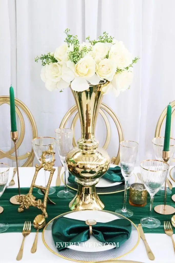 Green wedding theme table settings with sage green napkins, eucalyptus garland table runner, white candles, and gold charger plates for a rustic reception centerpiece idea