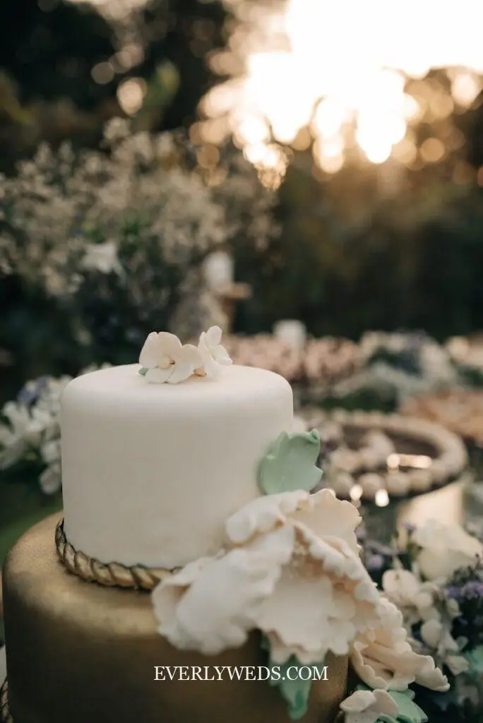 Simple white wedding cake with smooth buttercream finish on a wooden cake stand at a rustic wedding reception