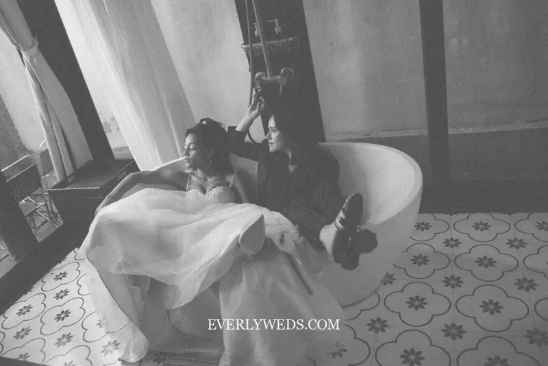 A couple sits in a bathtub wearing wedding attire.