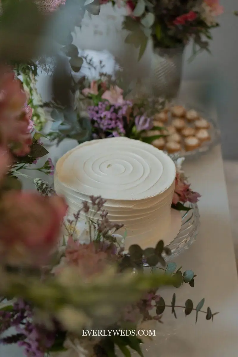 Simple one tier wedding cake with textured buttercream and minimal greenery on a ceramic stand, simple elegant wedding cake design