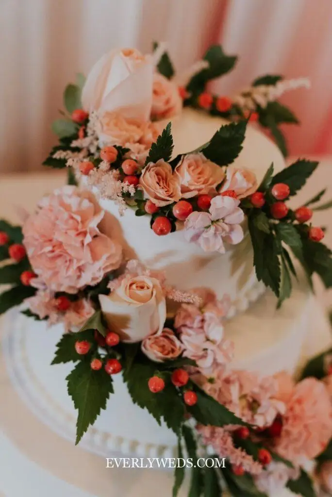 wedding cake design with fresh floral blooms roses and greenery cascading down white buttercream tiers