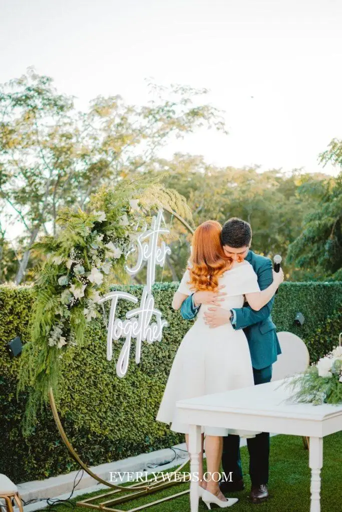 neon wedding sign glowing over sweetheart table with greenery wall backdrop, modern rustic wedding decor ideas reception