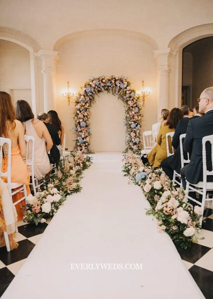 Wedding ceremony aisle with floral arch and guests seated.