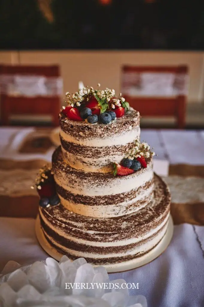 Naked simple wedding cake two tier design with visible cake layers and fresh berry topping at a rustic barn wedding reception
