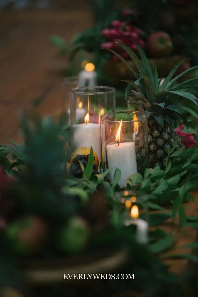 A table topped with lots of candles next to pineapples
