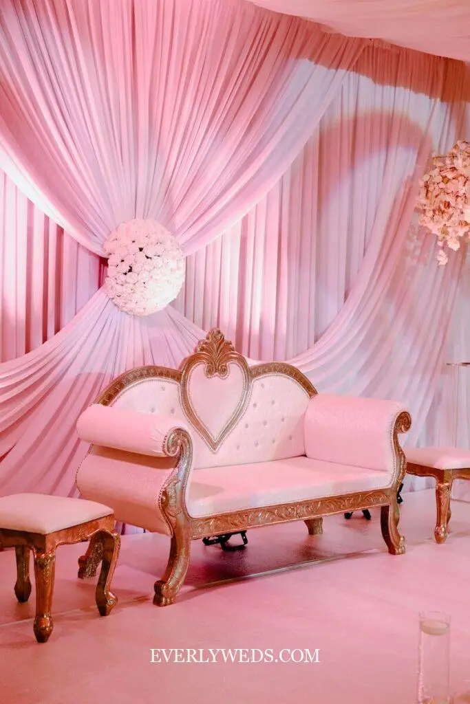 Pink draped fabric backdrop with ornate gold loveseat creates elegant budget wedding decor for small intimate ceremonies