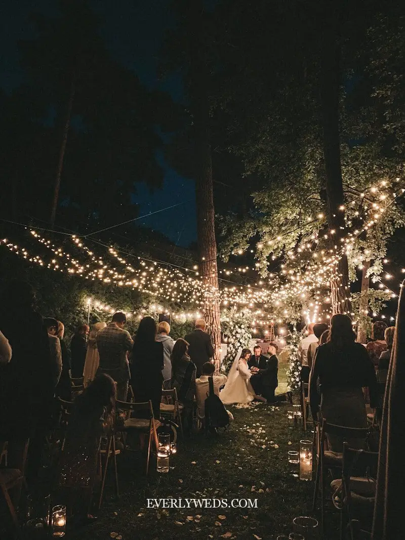 Unique wedding venue ideas modern summer camp wedding with string lights over outdoor dining tables and s'mores station